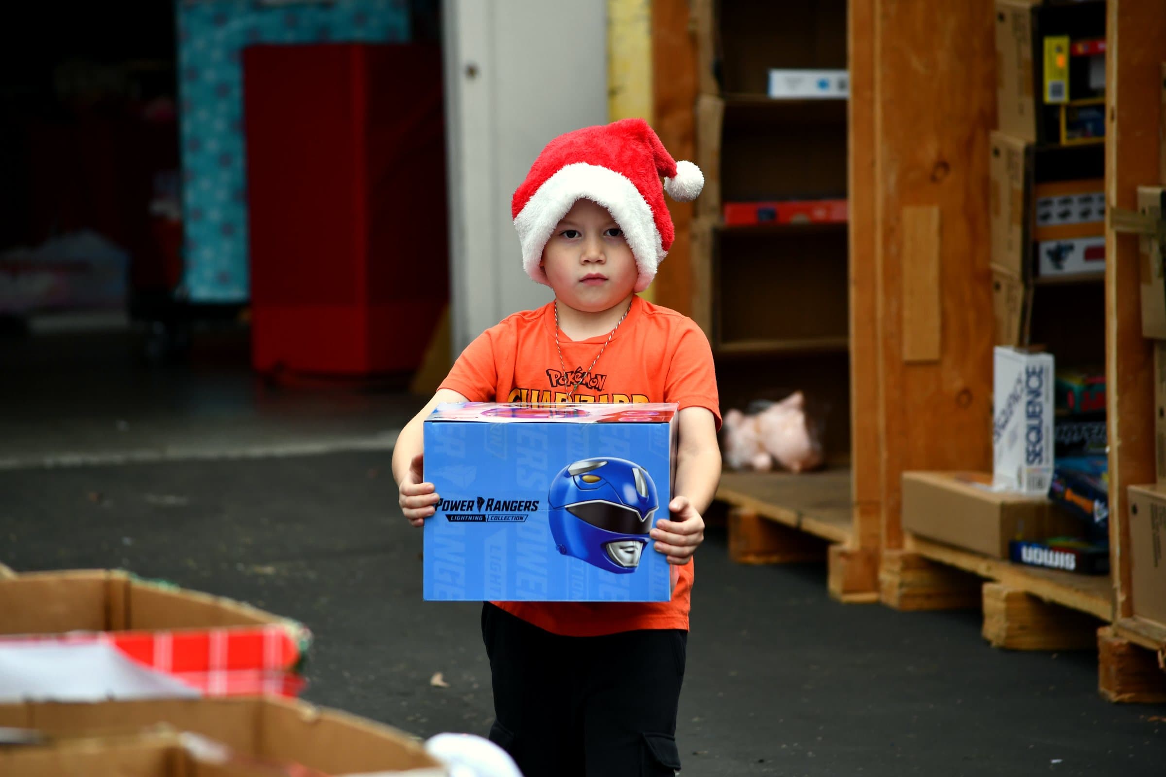 A young boy in a Santa hat carries the new toy he just received, walking out of the Joey's Toy Drive warehouse