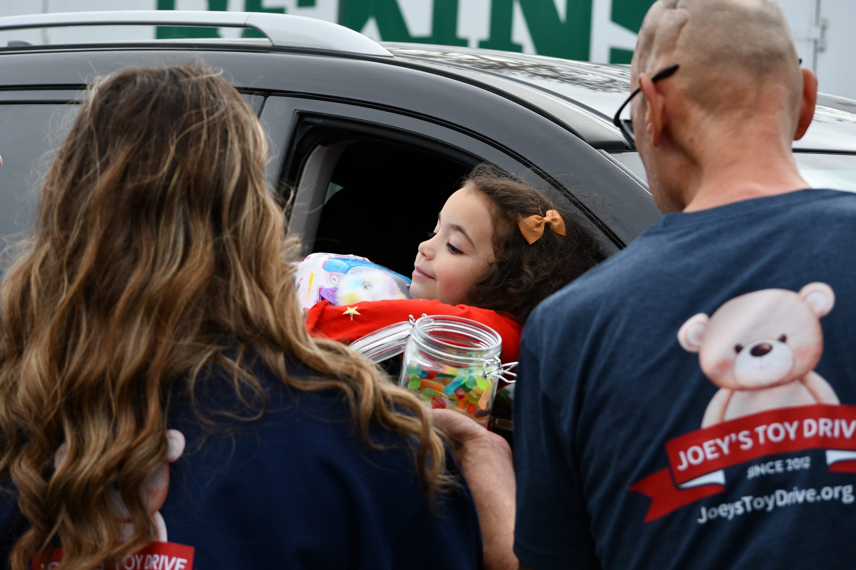 A volunteer hands a wrapped toy through a car window to a young girl reaching out for it on distribution day