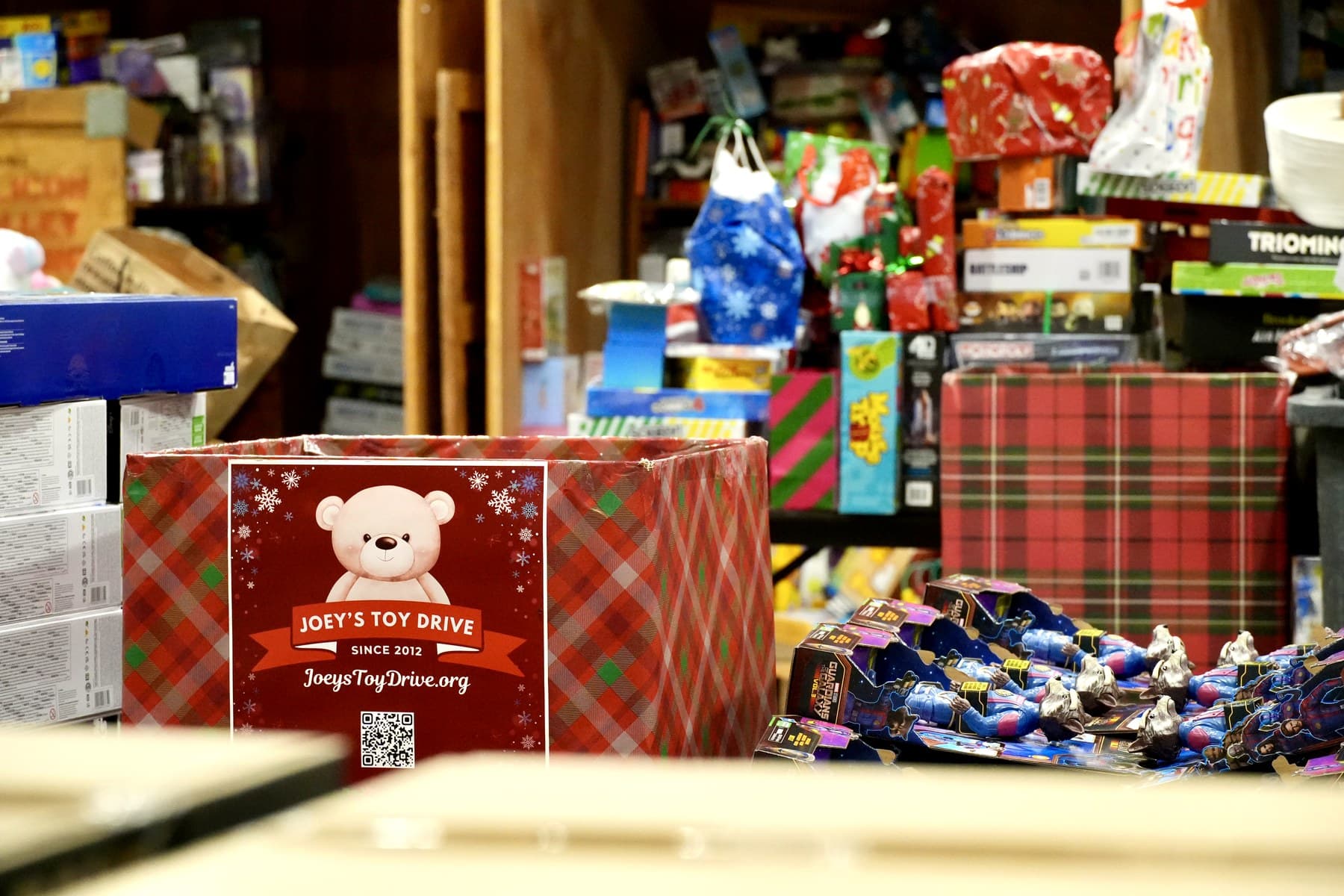 The Joey's Toy Drive warehouse mid-season, stacked with thousands of wrapped gifts beside a branded collection box